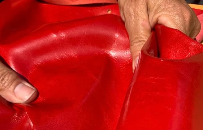 des mains qui manipulent une peau de cuir teinte en rouge dans un atelier de confection