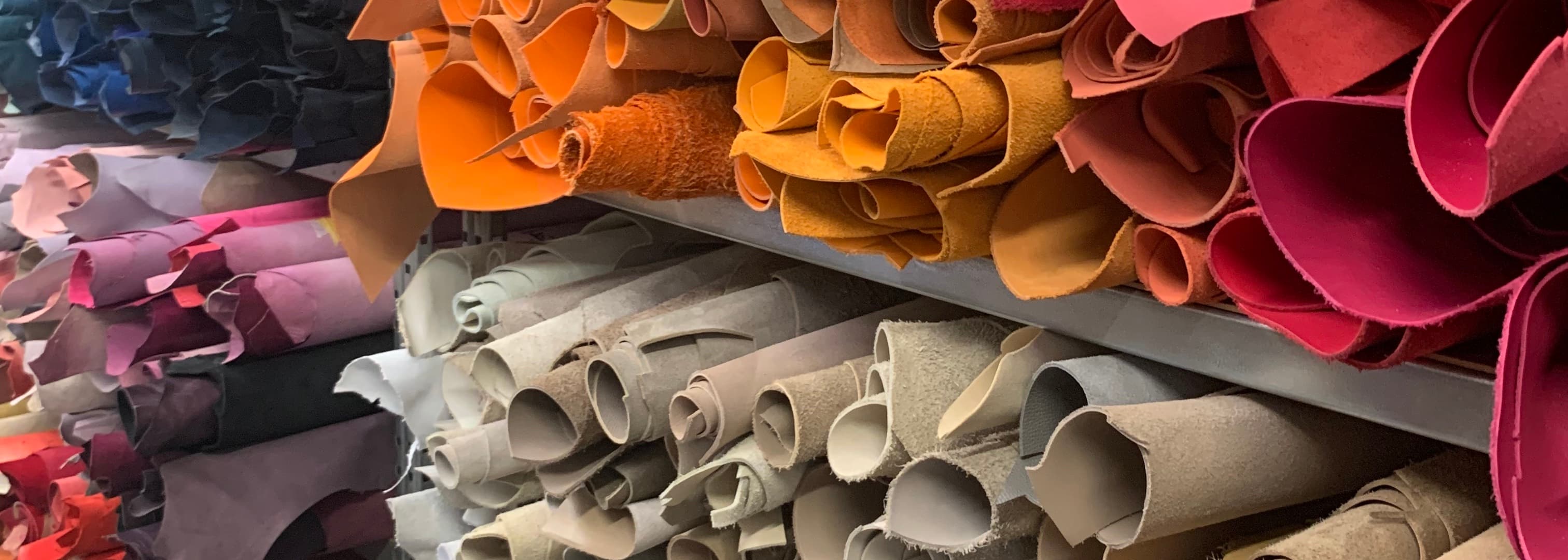 peaux de cuirs colorées et roulées sur des étagères dans un atelier de confection